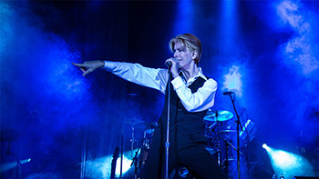 A musician passionately performing on stage under vibrant blue lighting, surrounded by musical equipment.