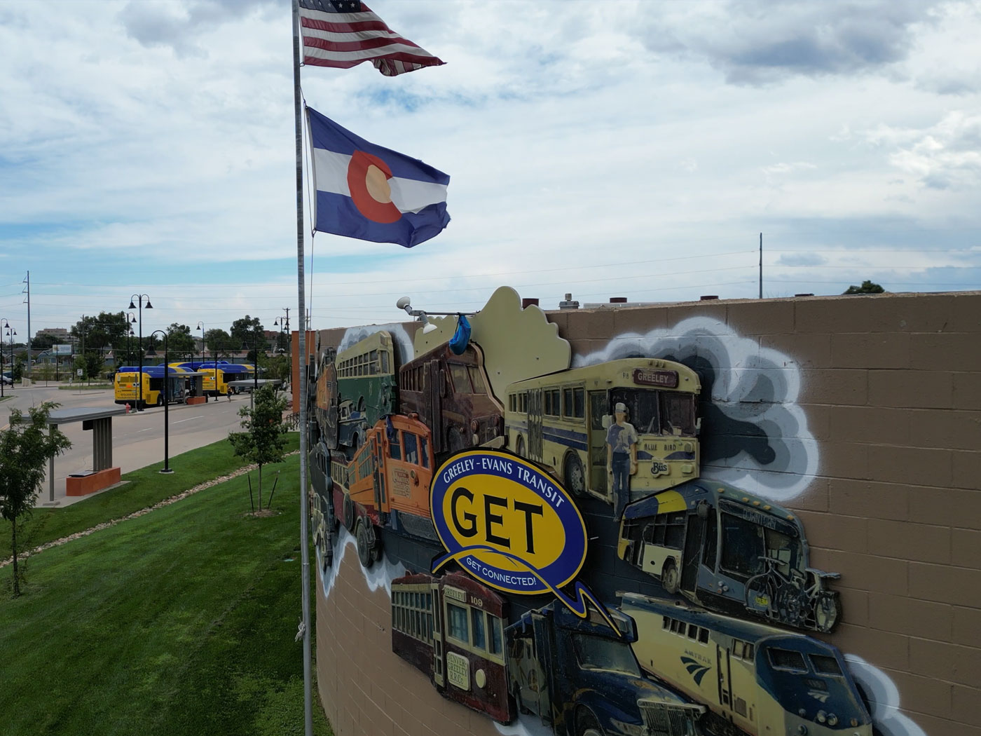 Outdoor shot of the GET headquarters building, featuring a mural with the GET logo and flagpole flying USA and Colorado flags and buses in the background