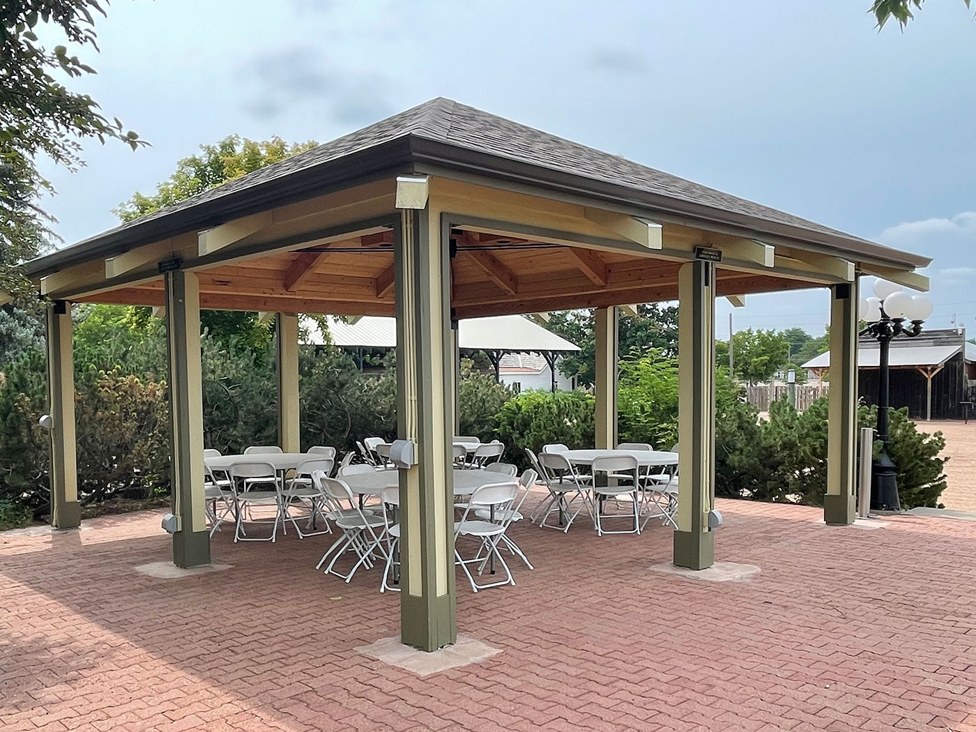 A rectangular pavilion shelters four circular tables with chairs on top of an expansive brick patio