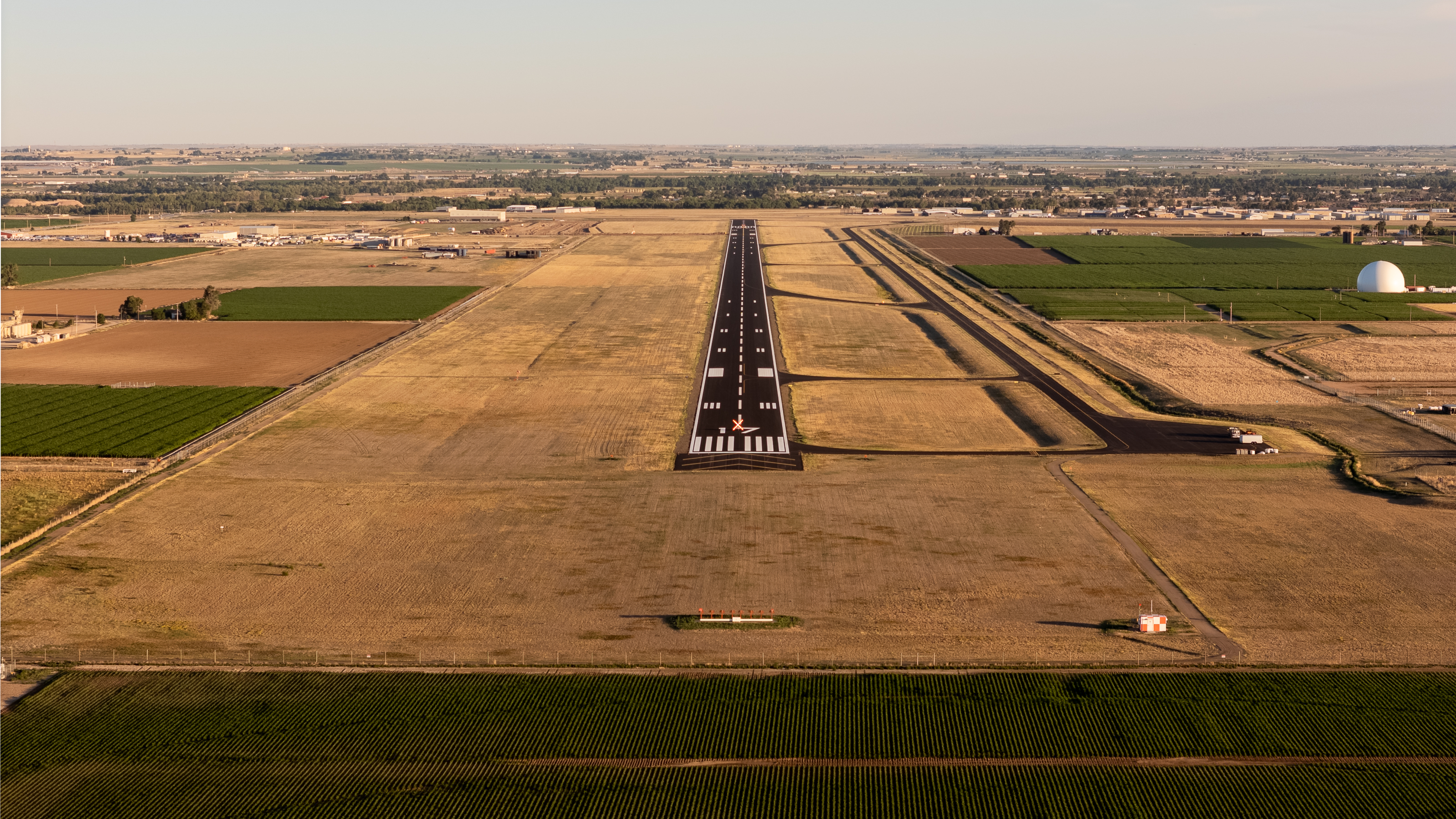 Aerial view of the Greeley-Weld County Airport runway surrounded by agricultural fields, airport facilities, and open plains in Greeley, Colorado.