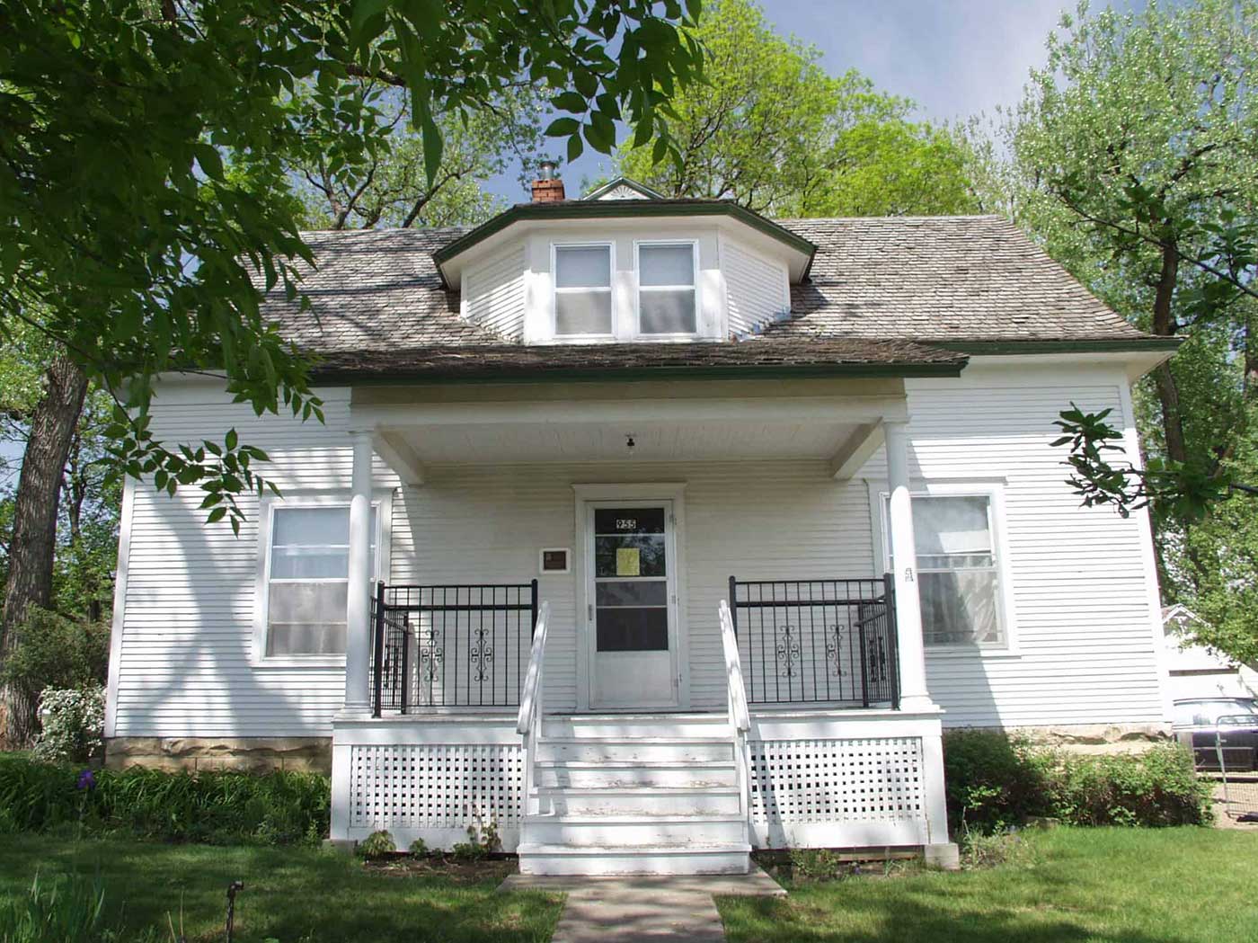 A charming historic white farmhouse surrounded by lush greenery and steep roof architecture, embodying rural heritage.