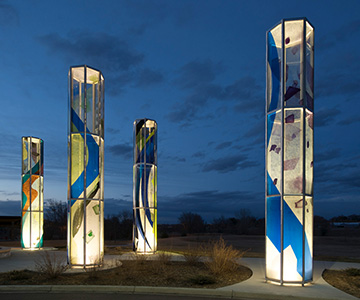 Four vertical installations featuring colorful designs lit against a twilight backdrop.