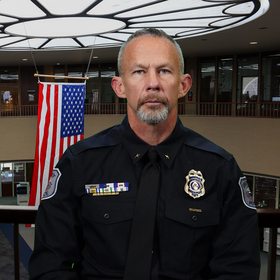 Commander David Wiles in formal attire with service decorations displayed, standing indoors near an American flag.