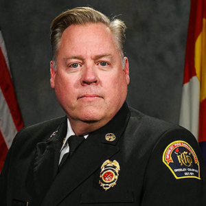 Portrait of a Greeley Fire Department official in uniform with the Colorado state flag in the background.
