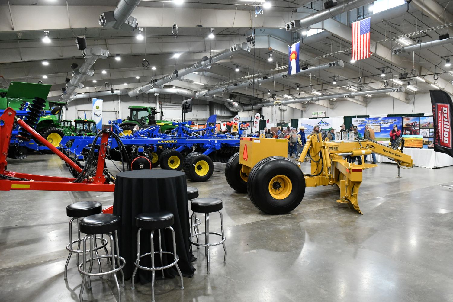 A brightly lit indoor space showcasing various large-scale farm equipment with attendees exploring exhibits.