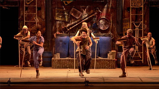 A group of performers showcasing dynamic movements on stage with props creating a lively and rhythmic atmosphere.