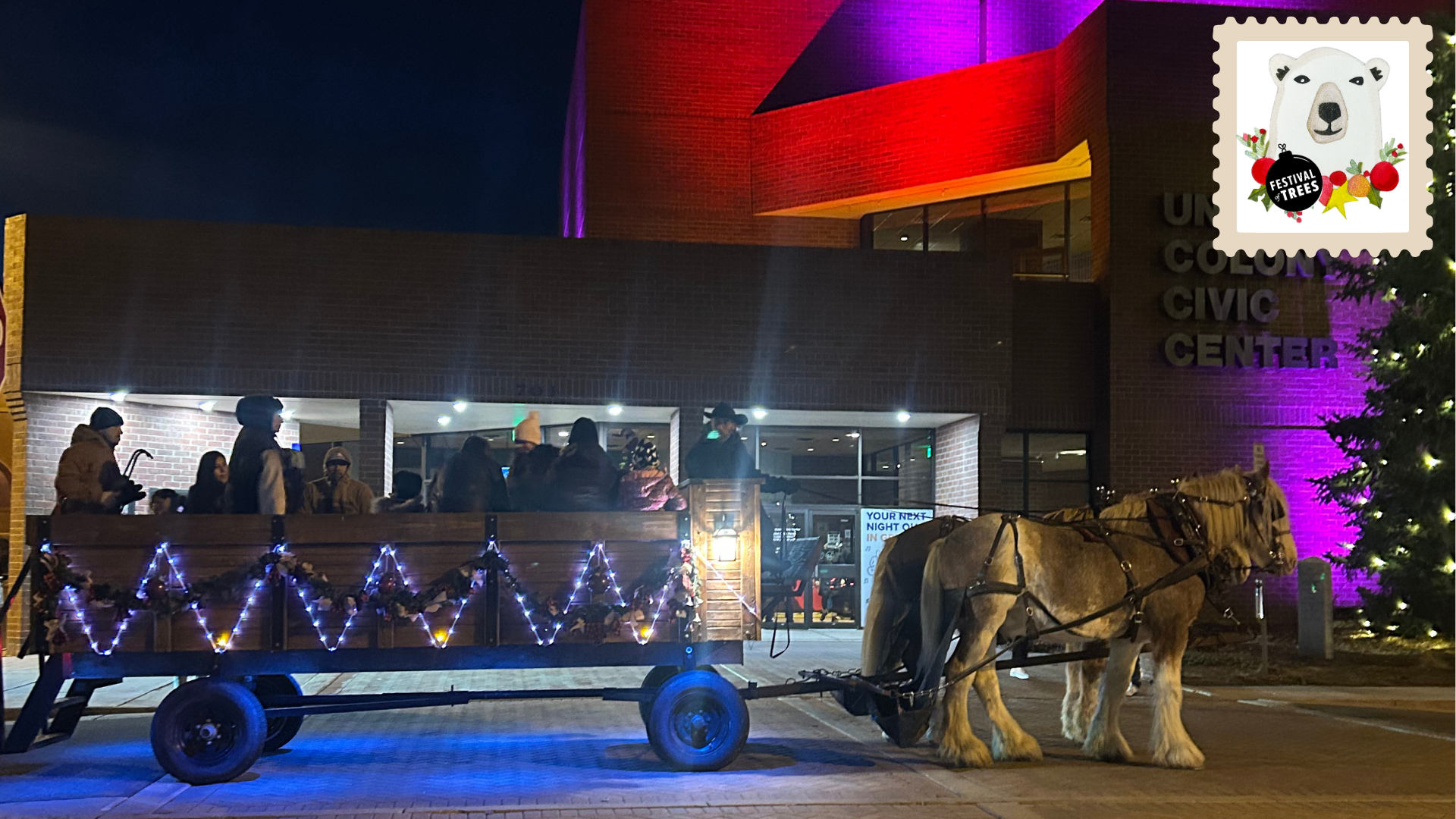Photo image of night scene in front of red and pink lit Union Colony Civic Center building with festive decorations on wooden wagon drawn by Belgian draft horses.