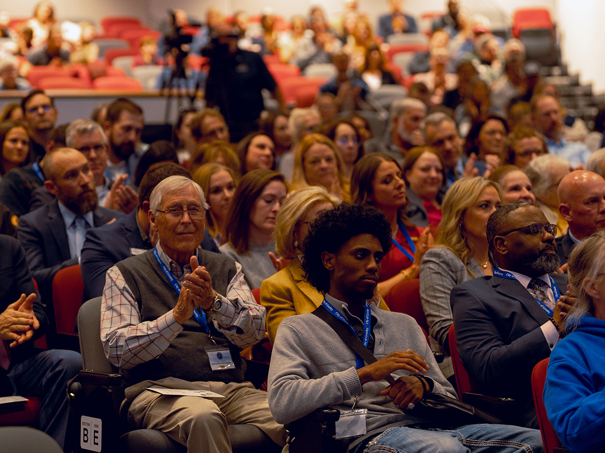 Attendees with lanyards at an event, sitting in auditorium and clapping