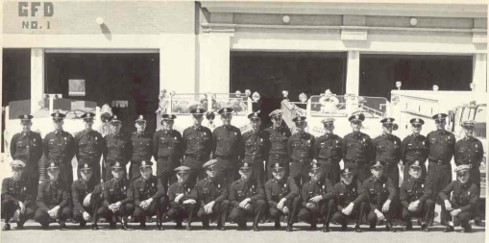A historical black and white group photo of the Greeley Fire Department taken in front of their station during the 1960s.