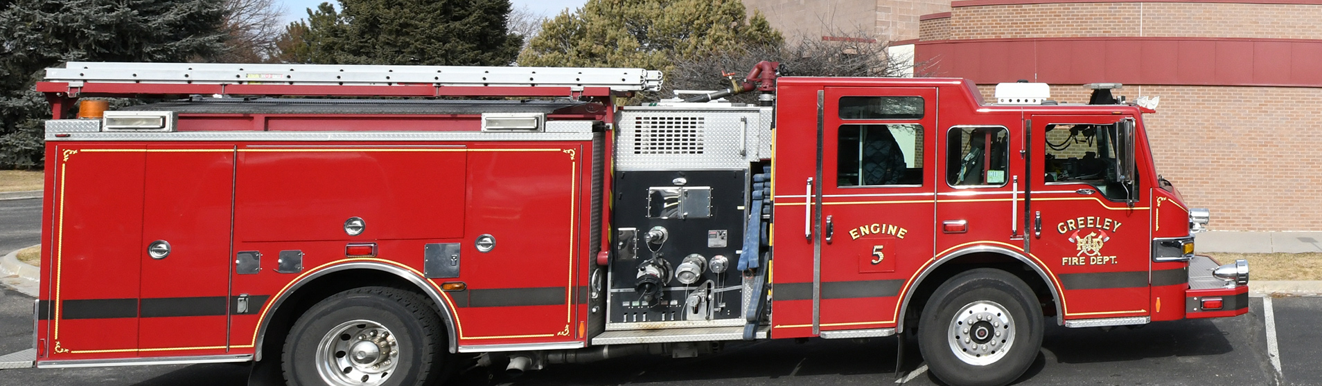 A red fire engine from the Greeley Fire Department, labeled as Engine Number Five, parked outdoors near a brick building.