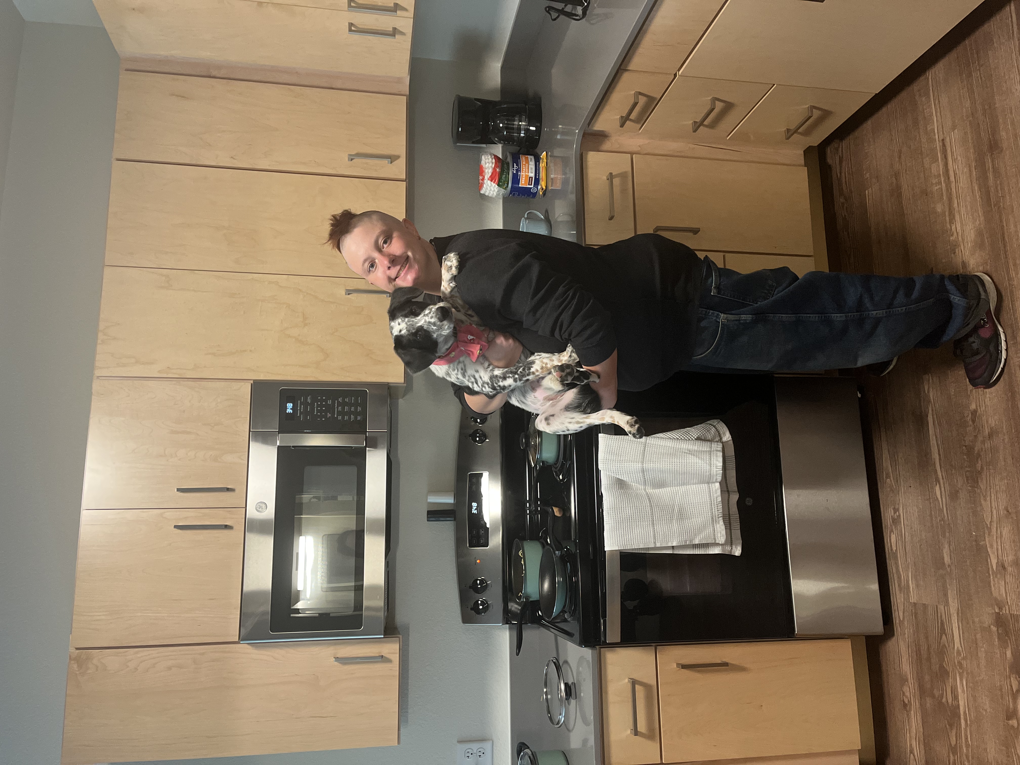 Sam holding dog, Itty Bitty who is medium and black and white, in his new apartment's kitchen at StarRise. 