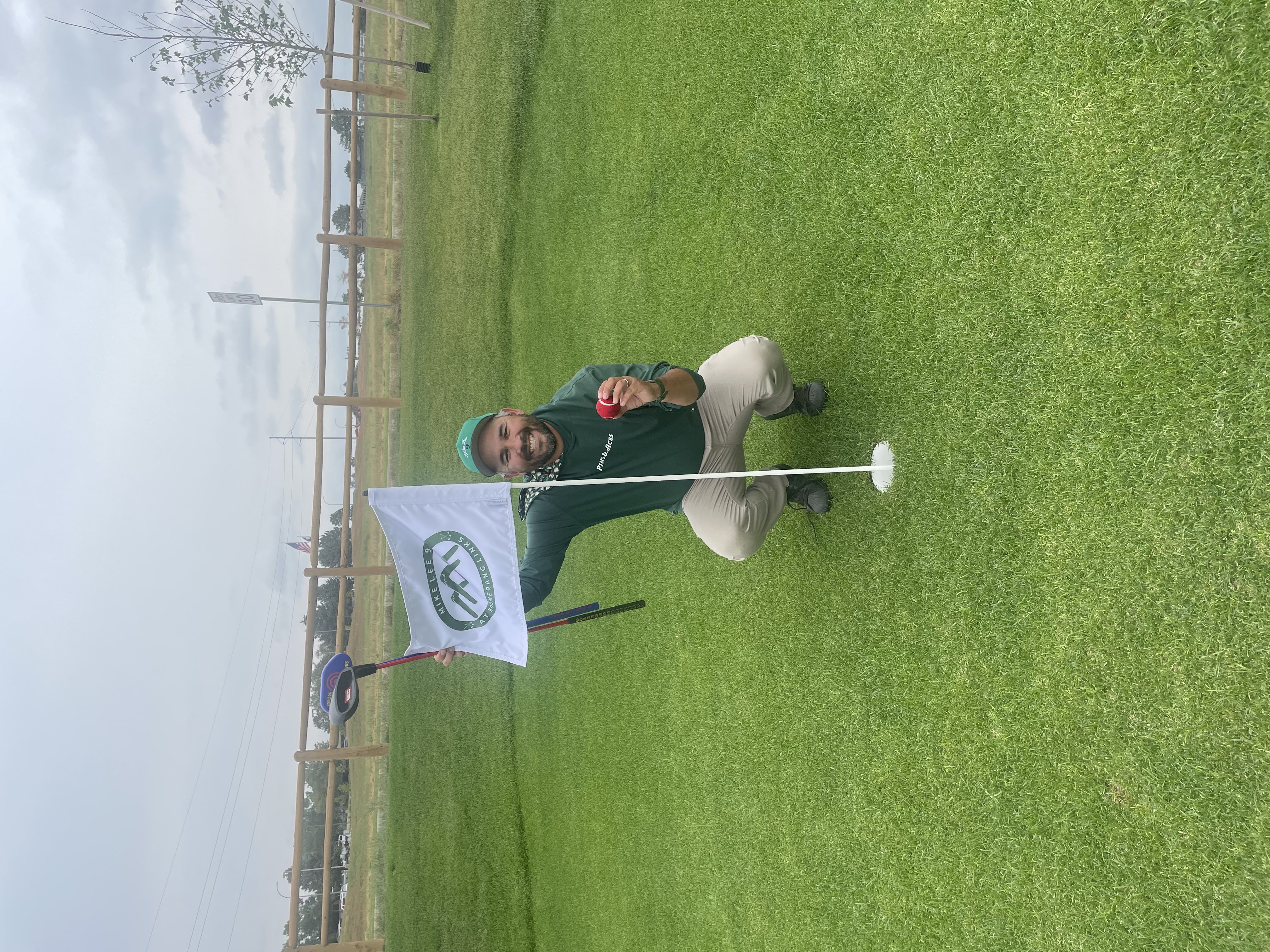 Golfer kneeling on the green holding a golf ball and flag after a hole-in-one on the short course at Boomerang Links
