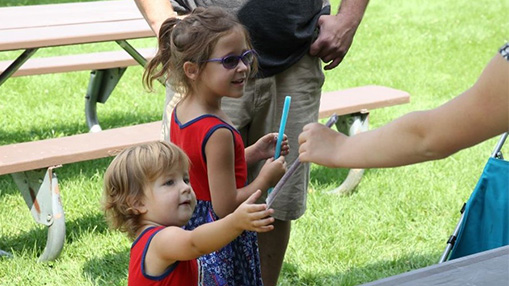 Children receiving popsicles at a community event with picnic tables in the background.