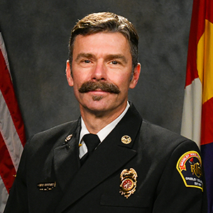 Image of a uniformed fire department official with flags in the background.