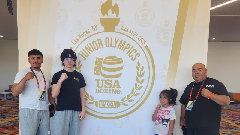Two boxers stand with their boxing coaches in front of the junior olympics banner at the las vegas convention center