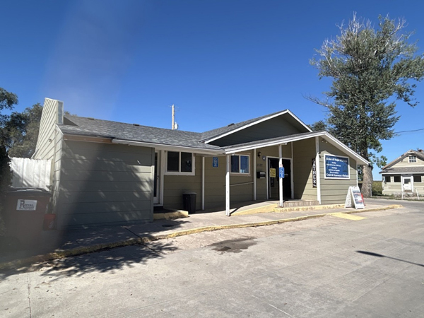 Single story framed building with parking spaces in front. 
