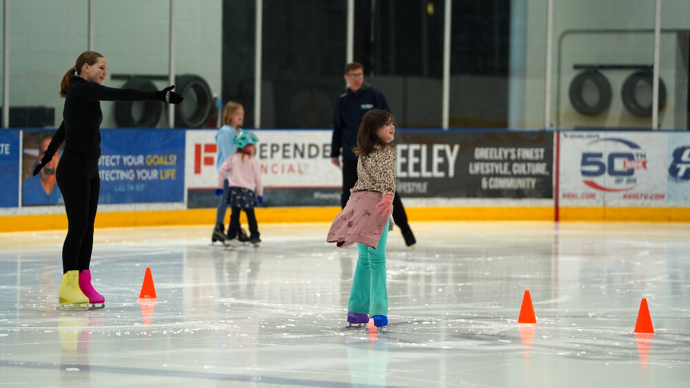 Two Learn to Skate instructors work with three students on the ice teaching ice skating lessons