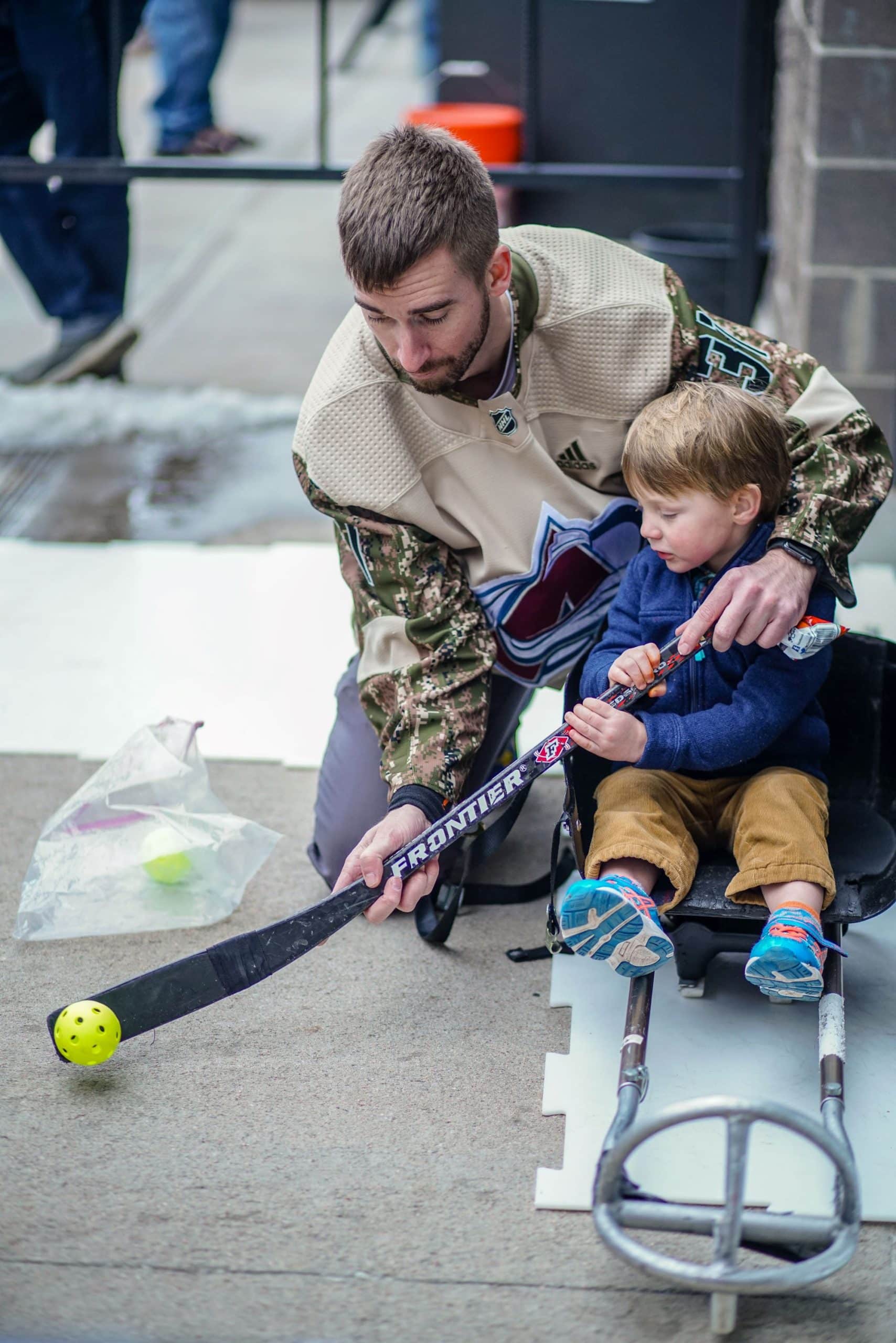 An instructor showcases sled hockey techniques to a young participant seated in a sled.