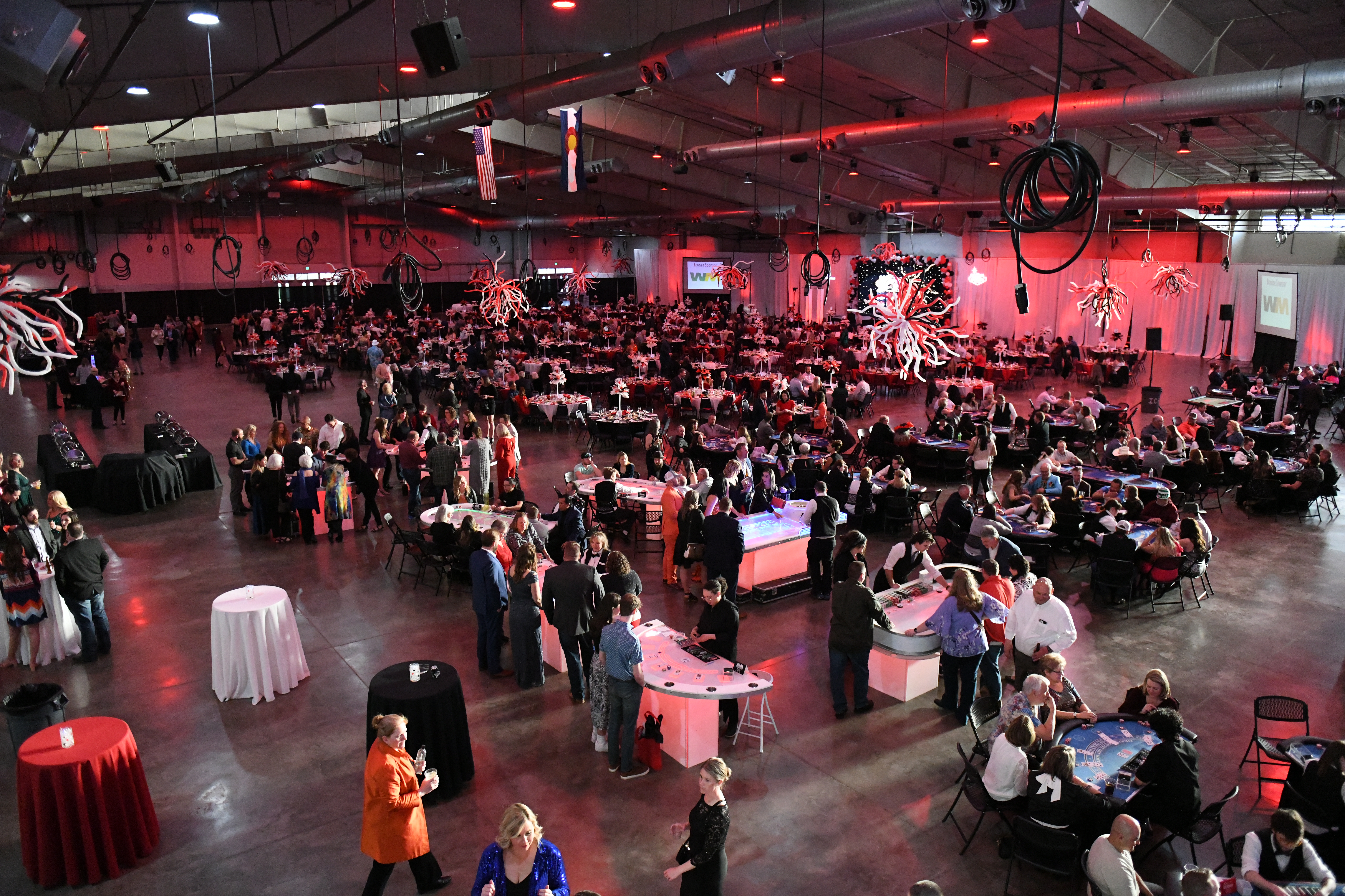 Well-dressed guests and card dealers gather around covered tables and a bar in an indoor banquet setting