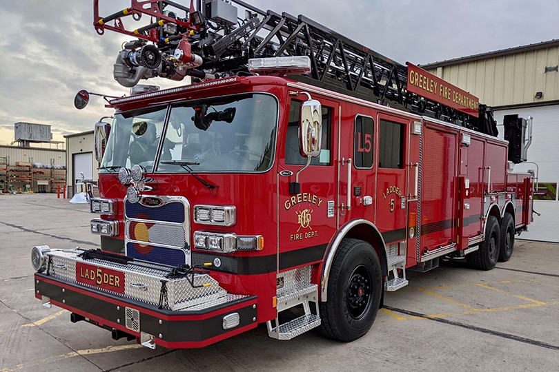 A vibrant red ladder truck from the Greeley Fire Department parked outside at the station, featuring modern firefighting equipment.