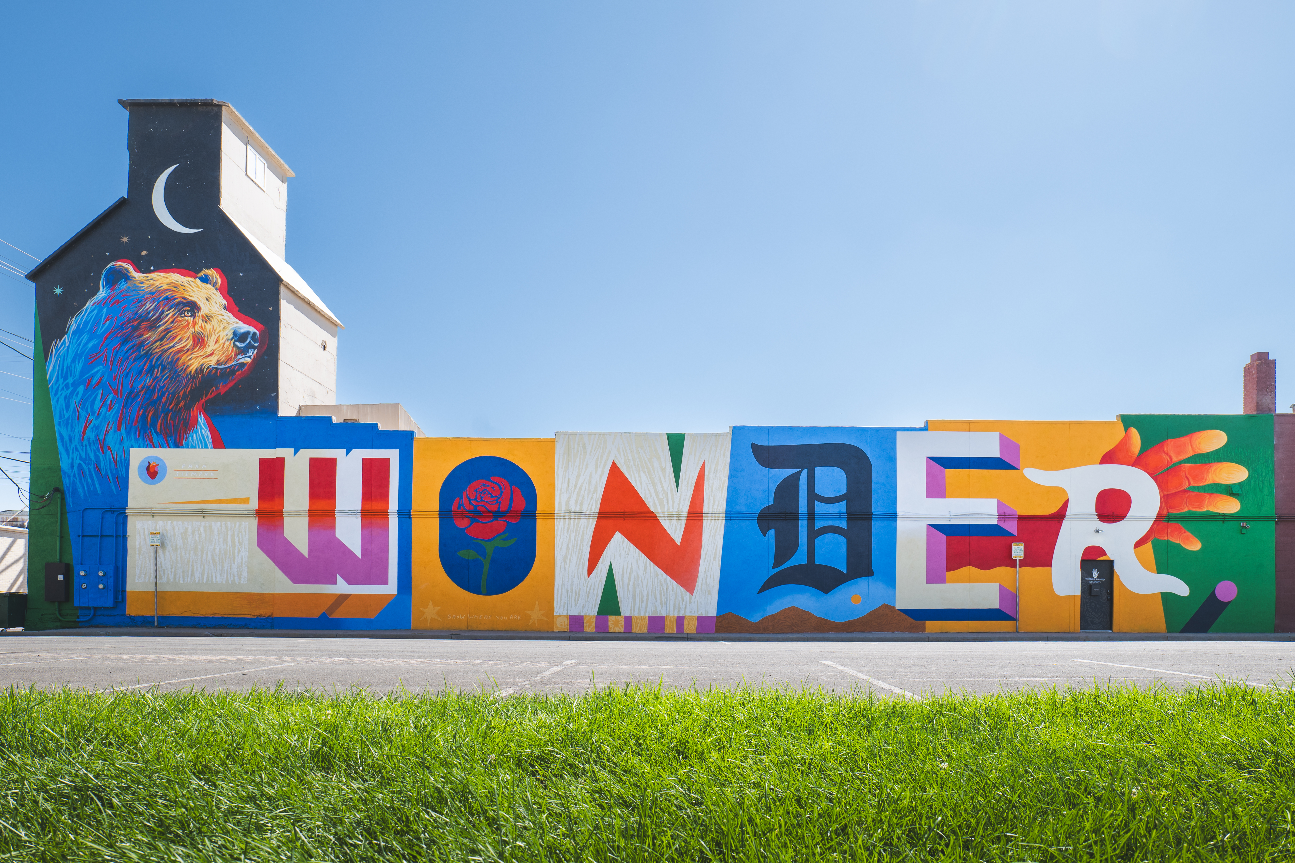 Picture of a mural, spelling "Wonder" in varying fonts, colors, and designs, on the side of a downtown Greeley factory building. Accompanying the "Wonder" text, to the left of the "W", is a painted picture of a bear. 