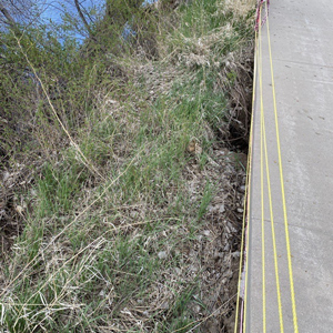 Image showcasing erosion along a riverbank causing separation between the paved trail and the bank.