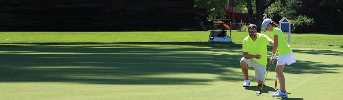 An instructor engaged in a one-on-one golf training session with a young participant on the green at a sunny golf course.