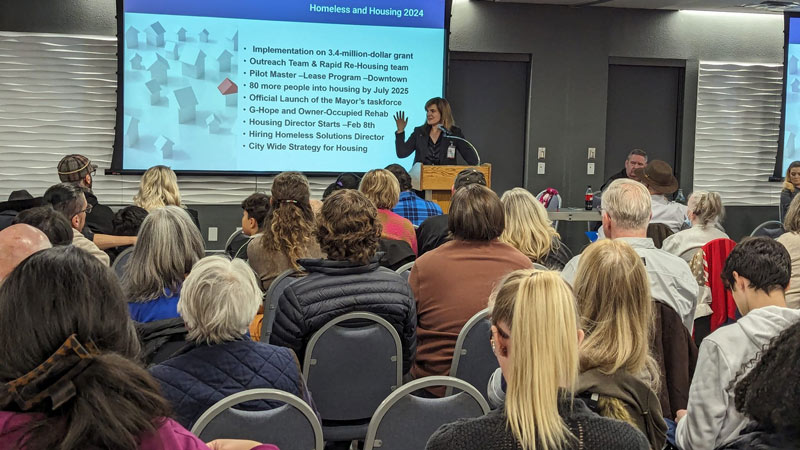 A woman addresses a crowd about upcoming housing and homelessness initiatives for 2024 and 2025.
