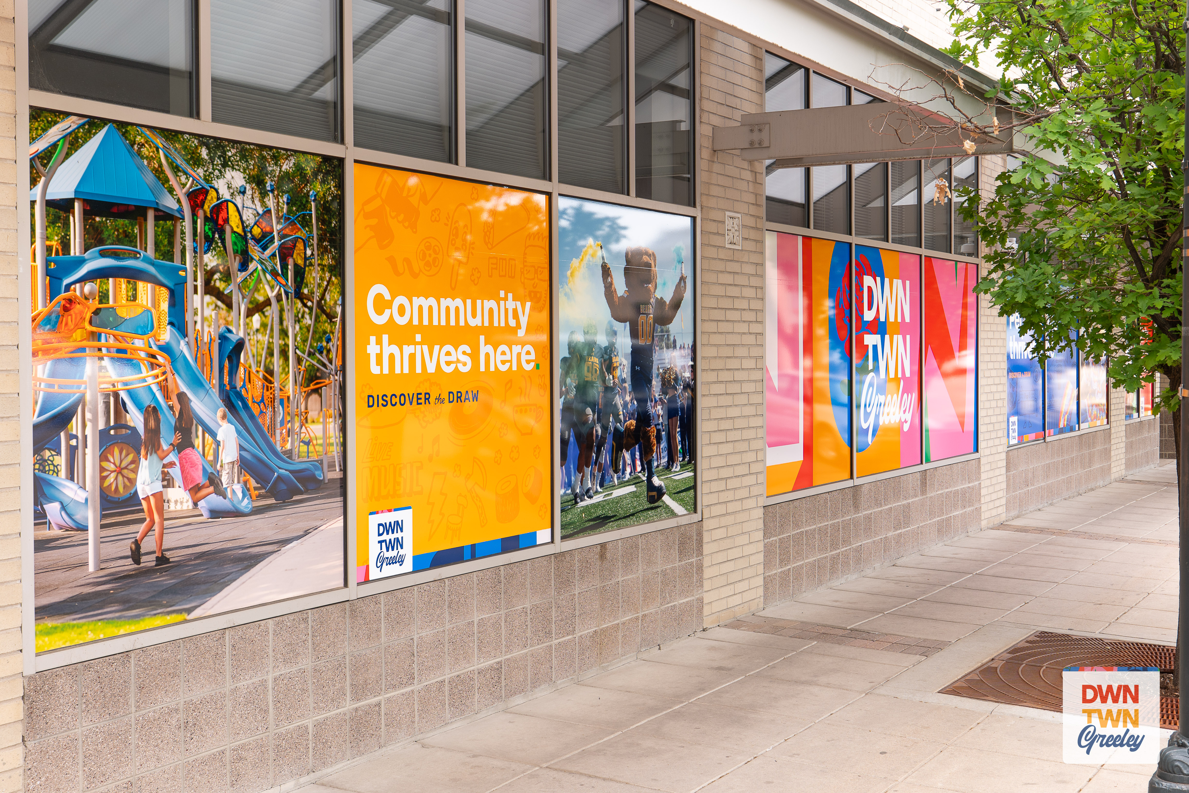 Picture of the front of vacant downtown businesses, with downtown Greeley branding facade on the windows, including pictures of parks and the UNC mascot.