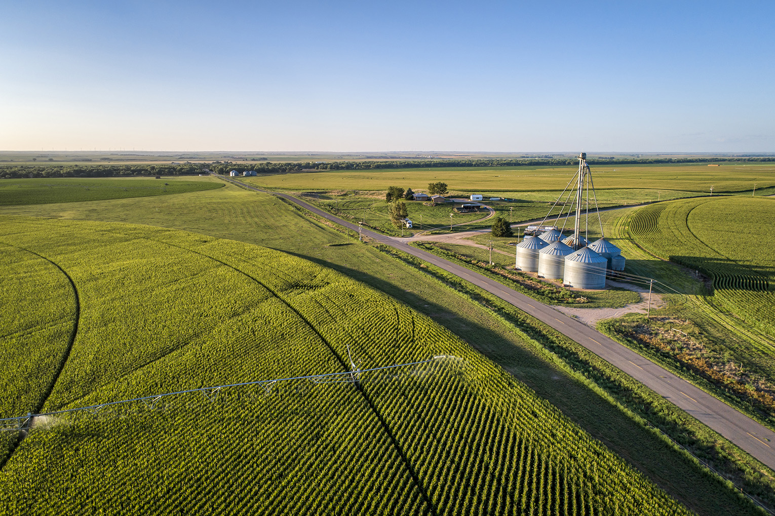 An expansive aerial view showcasing the vibrant green corn fields and modern silos in rural Colorado farmland.