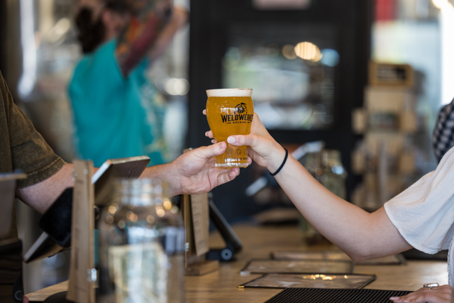 A person receives a glass of beer over a bar from a bartender.
