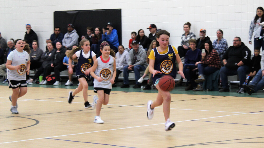 A young girl dribbles a basketball on a breakaway in an indoor court.