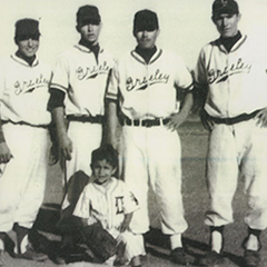 A group of Greeley Grays baseball players with their kneeling bat boy, showcasing team camaraderie.