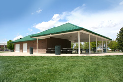 A spacious outdoor pavilion with green roofing, picnic tables, and open surroundings.