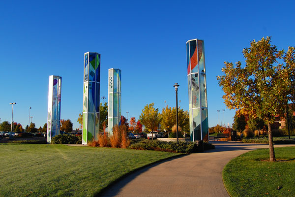 A scenic area showcasing tall, colorful glass pillars as part of a public art installation surrounded by trees and a park-like atmosphere.