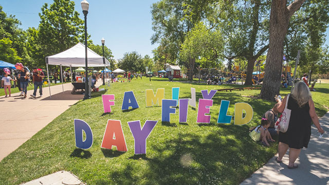 People walking around an outdoor park on a sunny day past pop-up tents and signage that reads Family Field Day
