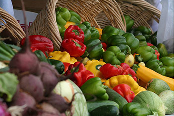 A vibrant display of fresh vegetables including peppers, beets, and squash laid out in woven baskets at a farmer's market.