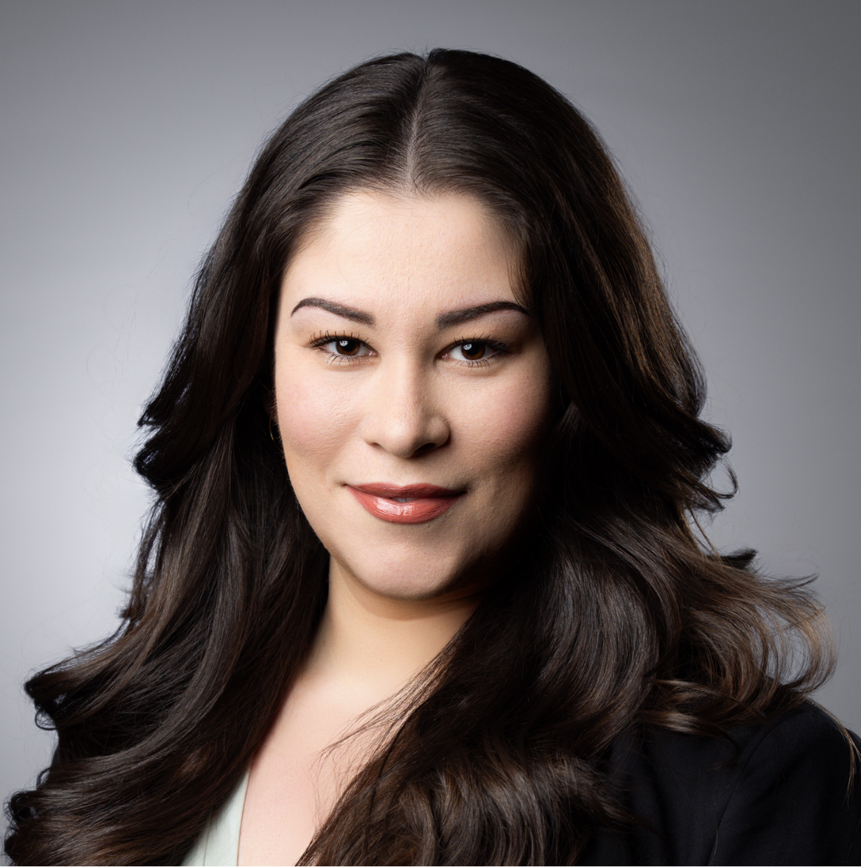 This image depicts a professional headshot of Real Estate Specialist Tania Gutierrez.  Tania is shown in a dark suit jacket with a silver colored v-neck blouse beneath.