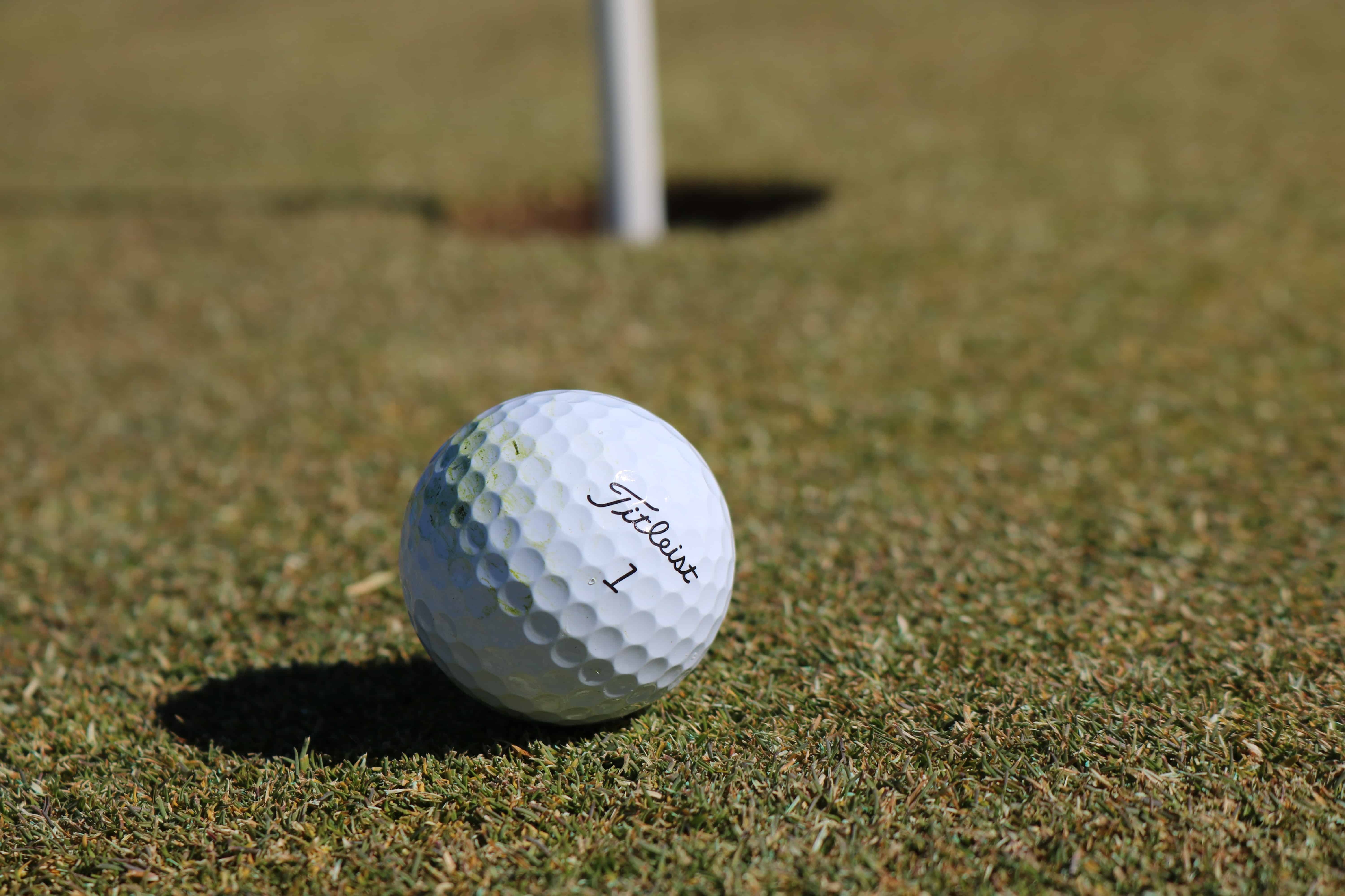 Close-up image of a Titleist golf ball on a pristine putting green with the hole in the background.