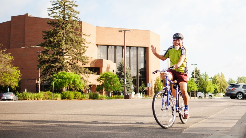 Man on a bike waving as he rides past the recreation center in Greeley