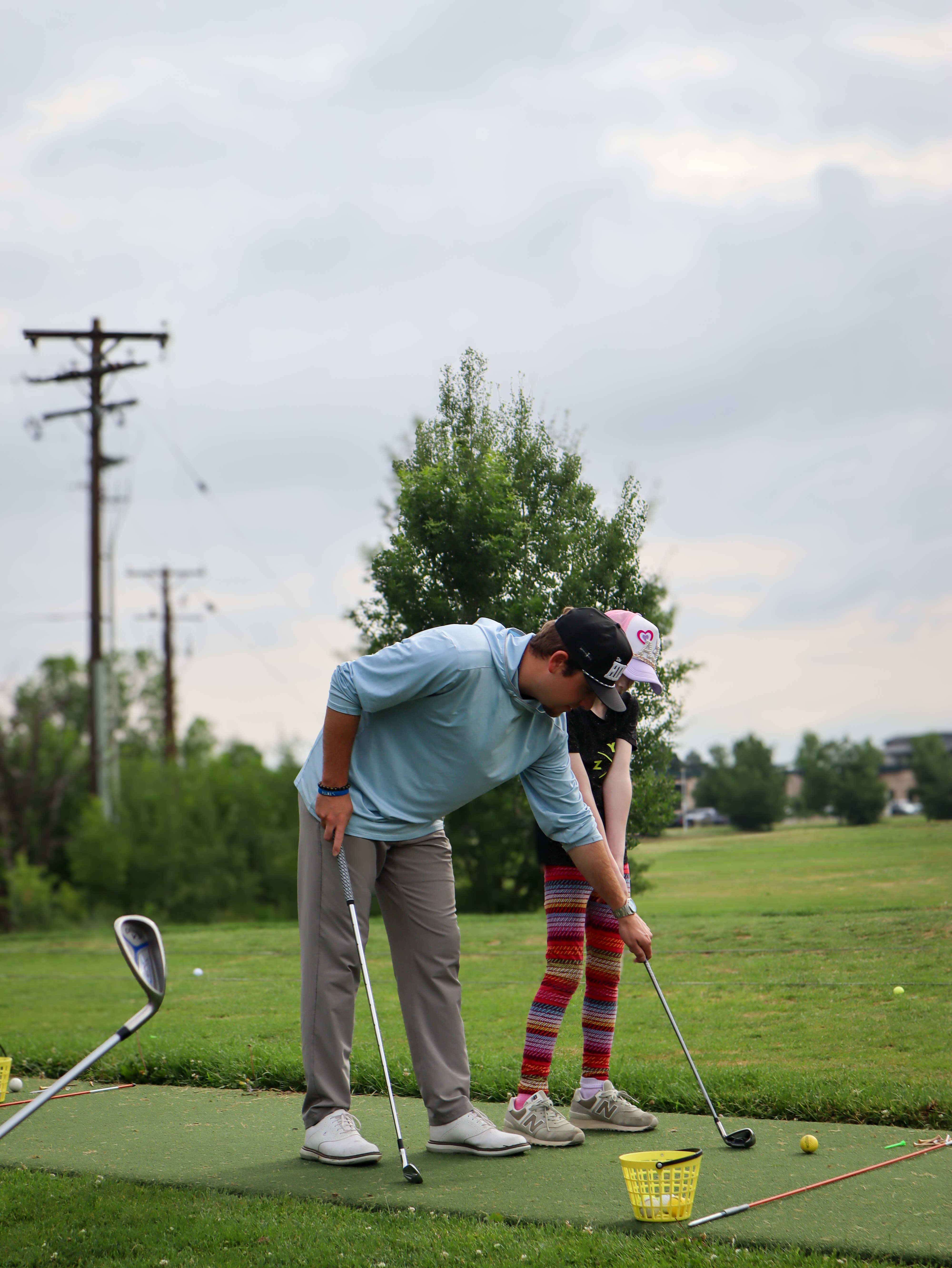 Golf instructor guiding a young golfer during a practice session atthe driving range.