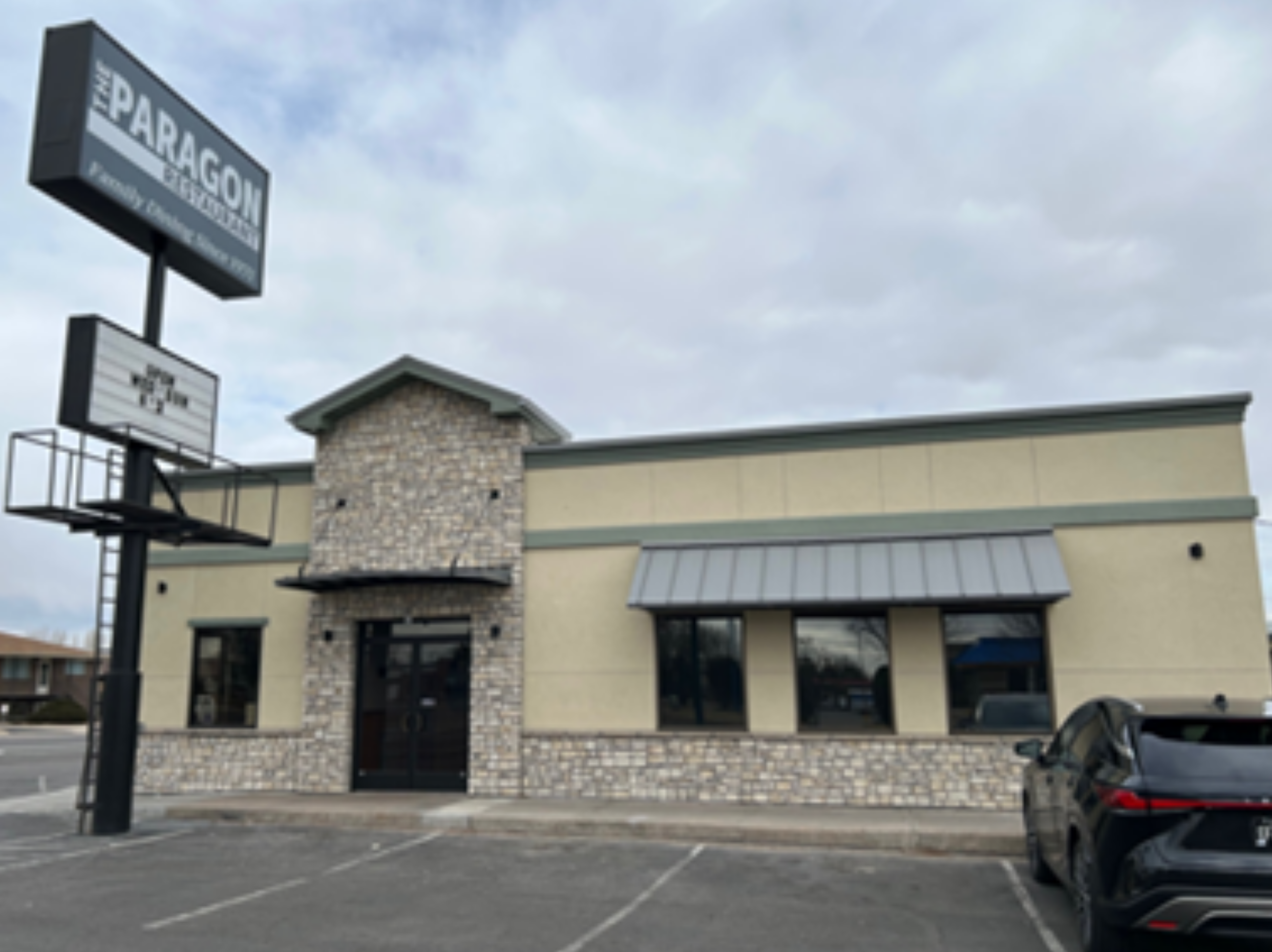 This image depicts the Paragon Family Restaurant in Greeley, Colorado, after a facade improvement project.  The updated exterior boasts gray stone under beige stucco.  A new metal green roof and awnings completes the updated stying, and a new, updated sign displays the name of the restaurant. 