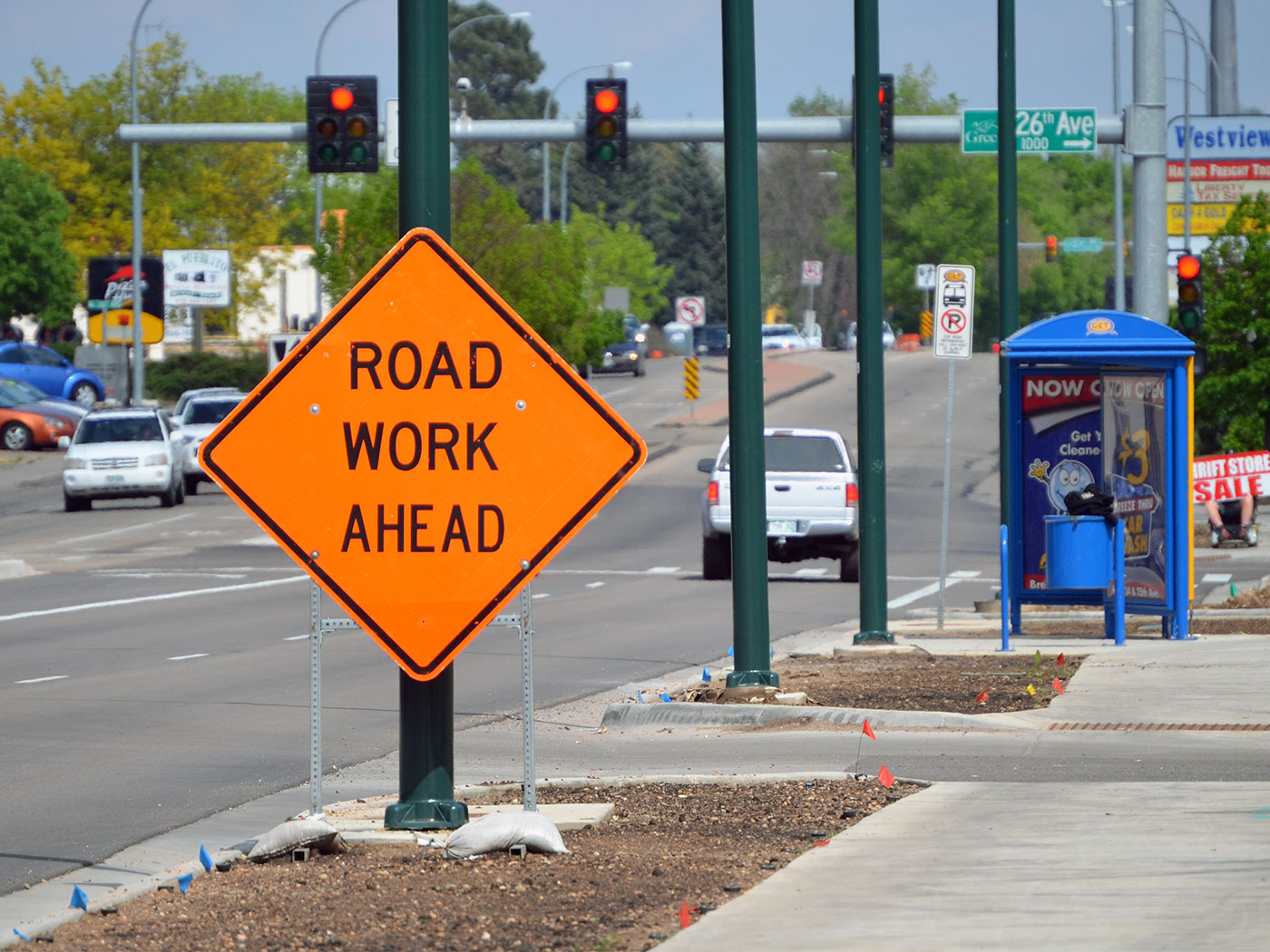 View of a street with a road work ahead sign in front of a bus stop