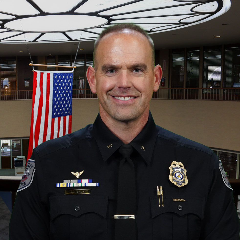 Commander Steve Fisher in formal attire with service decorations displayed, standing indoors near an American flag.