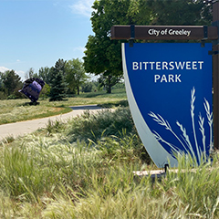 A serene park scene featuring greenery, sculptures, and a sign for Bittersweet Park in Greeley.