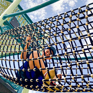 A child enjoys climbing through a rope tube structure on a modern playground.