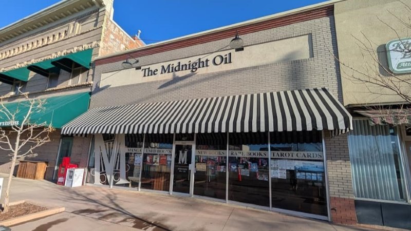 Front view of The Midnight Oil Bookstore, showcasing a striped awning and brick exterior facade.