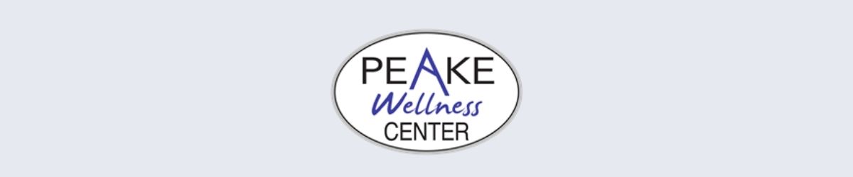 This image displays a logo with the words "Peake Wellness Center" inside an oval-shaped border. The letter "A" in the word Peake is set apart in purple and is stylized to look like a mountain peak.  The word "Wellness" is below the word "Peake" and is also set apart in purple letters that are written in script.  The remaining letters are in an uppercase sans serif font and are black in color.