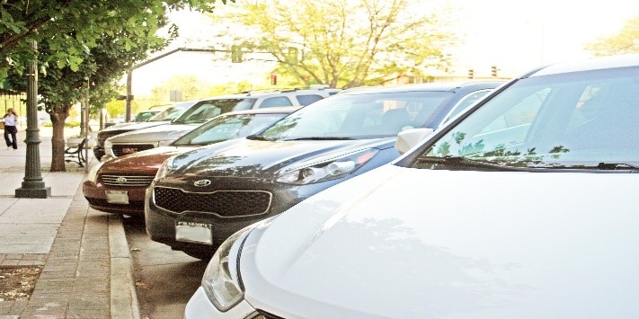 A view of cars parked along a city street with trees and urban infrastructure visible.