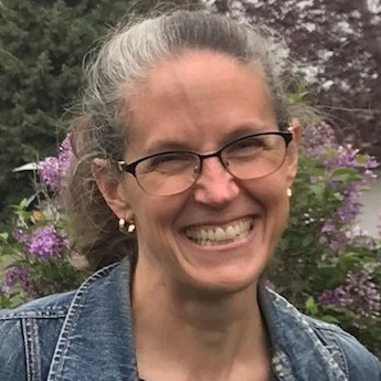 Elizabeth Kellums, City of Greeley Planner and Historic Preservation Specialist, photographed outdoors surrounded by greenery and lilac blooms.